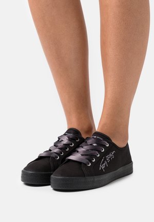 Baskets en toile noire avec lacets gris, semelle en caoutchouc et détails brodés sur le côté. Design bas, adapté pour un usage décontracté.