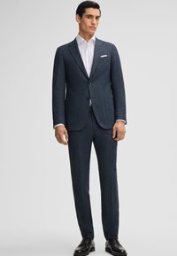 Completo su misura blu scuro con finitura testurizzata, dotato di giacca monopetto, revers a】notch e pantaloni coordinati, abbinato a una camicia bianca.