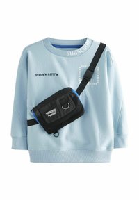 Gaiši zils džemperis ar apaļu kaklu un teksturētu audumu, kuram ir balti drukāti uzraksti. Ietver melnu plecu somu ar zilām akcentiem.