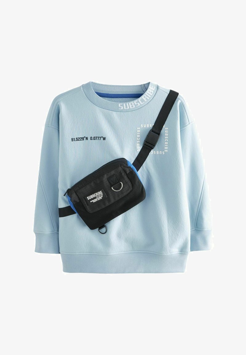 Gaiši zils džemperis ar apaļu kaklu un teksturētu audumu, kuram ir balti drukāti uzraksti. Ietver melnu plecu somu ar zilām akcentiem.