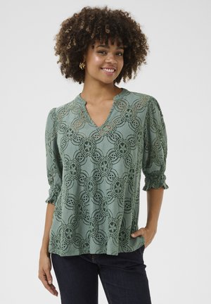 Blouse en dentelle vert sauge avec un motif floral, décolleté en V et manches trois-quarts froncées. Tissu doux avec une finition texturée.