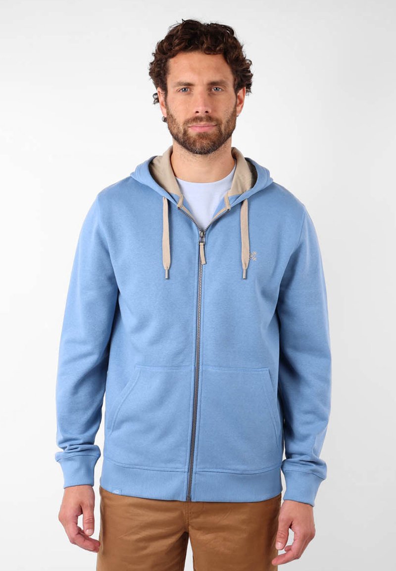 Haut de hoodie zippé bleu clair avec des cordons beiges, poches kangourou et poignets côtelés. Fabriqué en tissu doux, avec une coupe décontractée.
