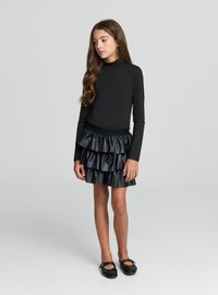 Top nero a maniche lunghe abbinato a una gonna nera in ecopelle con volant, caratterizzata da strati e vita elastica, completato da ballerine nere.