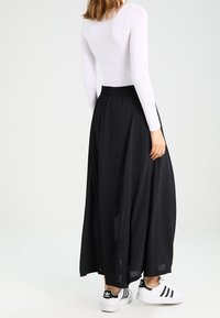 Svart maxikjol med en flödande design, tillverkad av lättviktig tyg. Kombinerad med en vit långärmad topp och svart-vita sneakers.