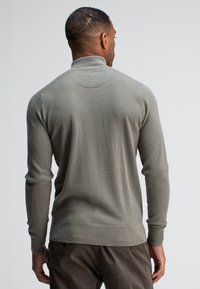 Grijze gebreide trui met een hoge kraag, textuurpatroon, aansluitende mouwen en een geribbelde zoom. Heeft een naadloos ontwerp aan de achterkant.