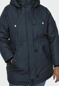 Marinblå isolerad parka med huva, som har en framsida med dragkedja, två sidfickor och silverfärgade detaljer. Mjuk textur och avslappnad passform.