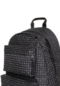 Mochila negra y gris hecha de un tejido texturizado que presenta un patrón de cuadrícula, bolsillos externos con cremallera y un asa de agarre en la parte superior.