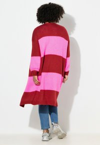 Cardigan lavorato a maglia con ampie righe orizzontali in rosso scuro e rosa brillante, caratterizzato da una vestibilità comoda, maniche lunghe e lunghezza fino a metà coscia.