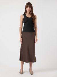 Svart ripset tanktopp kombinert med et middels langt brunt satengskjørt, med en glatt tekstur og myk fall. Nøytrale sko fullfører antrekket.