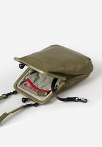 Olivgrüner Lederbeutel mit einem Reißverschluss Öffnung, gestreiftem Innenraum, roter Akzenttasche und abnehmbaren Tragegurten. Kompakte und strukturierte Gestaltung.