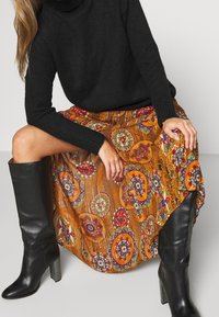 Maglione nero a collo alto con maniche lunghe abbinato a una gonna colorata a fantasia con motivi circolari in arancione, rosso e blu. Stivali neri sopra il ginocchio.