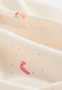 Tissu crème avec une texture côtelée présentant des motifs colorés brodés d'un cône de crème glacée et d'une canne en sucre rouge, entourés de petits points.