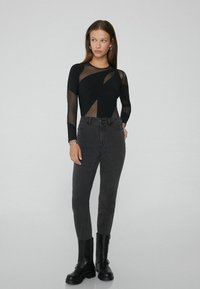 Černý body s dlouhým rukávem a síťovanými prvky, kombinovaný s černými džínami s vysokým pasem a černými robustními botami. Elegantní a přiléhavý design.