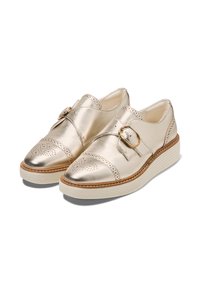 Guldmetalliska läderskor med rundad tå, perforerat mönster, justerbar rem med rund spänne och en vit platt sula.