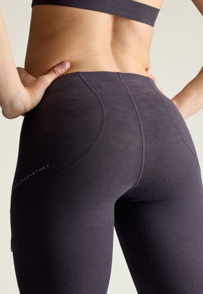 Nahaufnahme einer Person, die dunkle enganliegende Leggings und einen Sport-BH trägt, die Hände auf den Hüften ruhend, zeigt den unteren Rücken und die Oberschenkel.