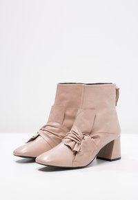 Beiga läderankelstövlar med spetsig tå, knuten detalj framtill och en kraftig klack. Slät yta och dragkedja bak för lätt påtagning.