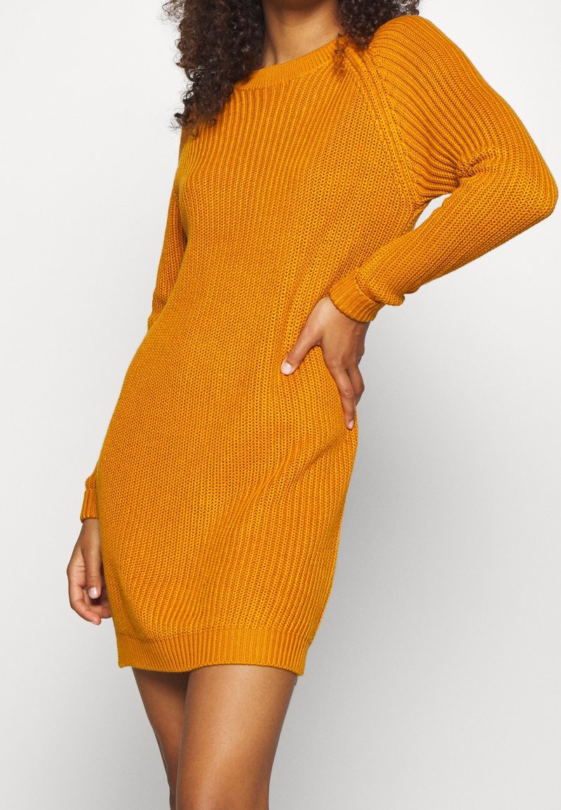 Koftklänning i senapsgul, med långa ärmar, ribbad textur, rund halsringning och figurnära design med en fåll vid mitten av låret.