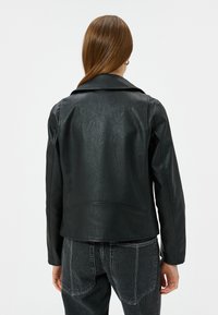 Zwart leren jack met een gestructureerde afwerking, voorzien van een klassieke kraag en een rechte snit, gecombineerd met donkere jeans. Achteraanzicht weergegeven.