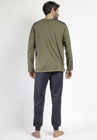 Camisa de manga larga verde olivo con toques en navy en los hombros, combinada con joggers oscuros en navy que cuentan con puños elásticos y un ajuste relajado.