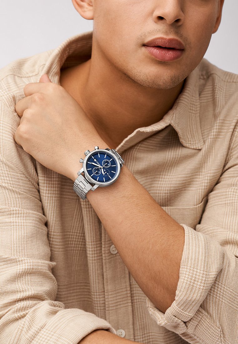 Blaues Chronograph-Uhr mit silbernem Metallarmband und rundem Gehäuse, das drei Hilfszifferblätter, ein strukturiertes Ziffernblatt und polierte Hardware aufweist.