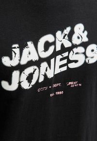 Sort t-shirt med stort, slidte hvid tekst med teksten "JACK & JONES" samt mindre pink tekst nedenfor. Blødt, bomuldsstof med en afslappet pasform.