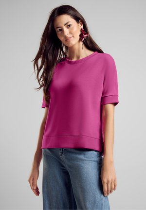 Fuchsia short-sleeve top with a round neckline, featuring a relaxed fit and folded cuffs. Paired with light blue wide-leg jeans.