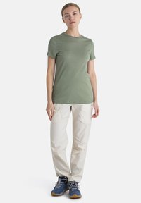 T-shirt verde chiaro a maniche corte, dal tessuto morbido; abbinato a pantaloni cargo chiari e sneakers blu con lacci grigi e suole marroni.