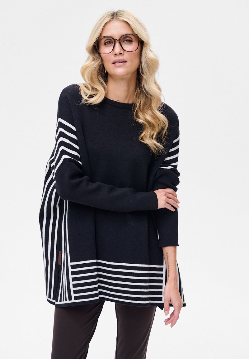 Czarny sweter z białymi poziomymi paskami, luźny fason, miękka faktura i boczne rozcięcia, zestawiony z ciemnymi spodniami.