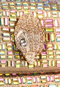 Clutch dorato con decorazioni simili a gemme colorate, dotato di un accento a forma di conchiglia adornato con strass trasparenti e una superficie texturizzata.