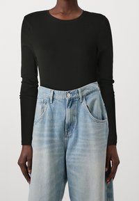 Schwarzes langärmliges Shirt kombiniert mit hellblauen hochgeschnittenen Jeans aus Denim, ausgestattet mit Fronttaschen und einem lockeren Schnitt.