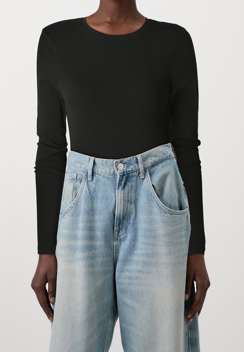 Schwarzes langärmliges Shirt kombiniert mit hellblauen hochgeschnittenen Jeans aus Denim, ausgestattet mit Fronttaschen und einem lockeren Schnitt.