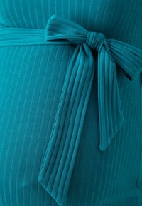 Teegrünes, geripptes Kleid aus Stoff mit einer Schleife in der Taille, das ein strukturiertes Muster und ein weiches, dehnbares Material zeigt.