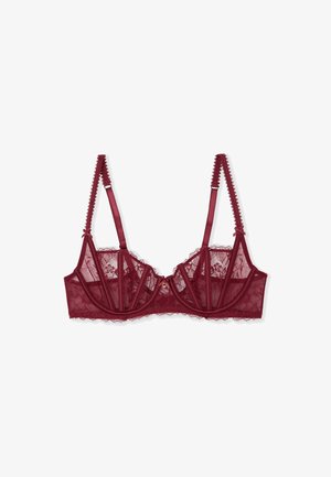 Reggiseno in pizzo bordeaux con coppe trasparenti, cuciture strutturate, spalline in raso e bordi smerlati. Al centro frontale presenta un piccolo dettaglio decorativo.