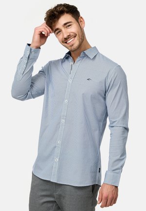 Camisa de botones azul claro con un pequeño patrón de cuadros, de manga larga y con un collar clásico. Presenta un logo en el pecho y botones blancos.