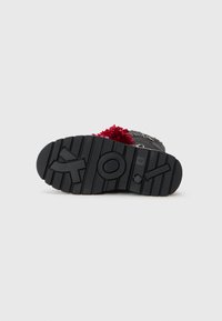 Suola di scarpa in gomma nera con un motivo testurizzato, accentuato da rilievi e dettagli con logo circolare. Decorazione con pom-pom rosso sul lato.