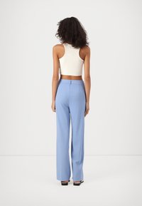 Pantalon large bleu clair en tissu doux, avec une taille haute et une texture lisse, associé à un débardeur blanc court.