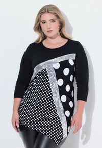 Černý top s kombinací bílých puntíků a stříbrných flitrů, tříčtvrteční rukávy a asymetrický lem.