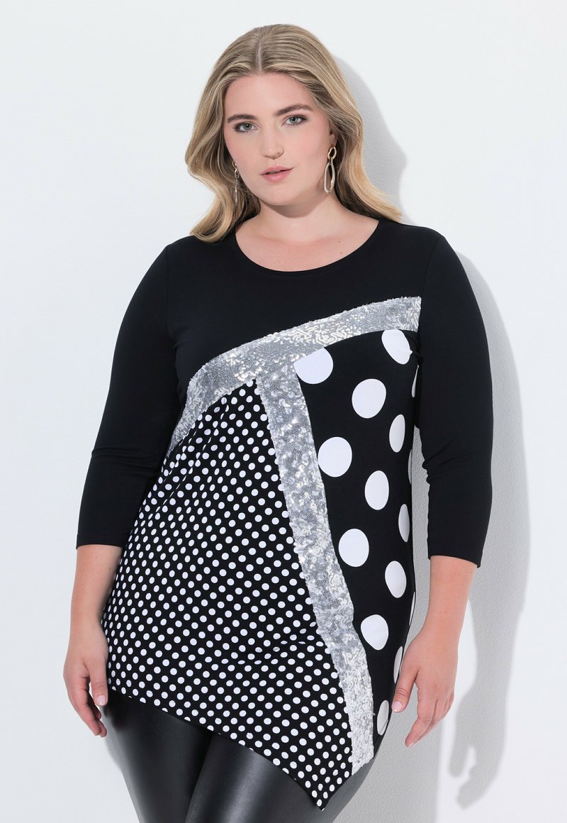 Černý top s kombinací bílých puntíků a stříbrných flitrů, tříčtvrteční rukávy a asymetrický lem.