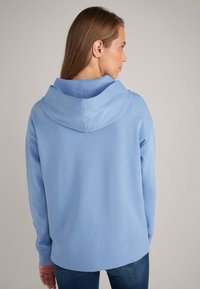 Felpa leggera blu con cappuccio regolabile, maniche lunghe e vestibilità rilassata, realizzata in un tessuto morbido e testurizzato. Dettagli di cucitura visibili.