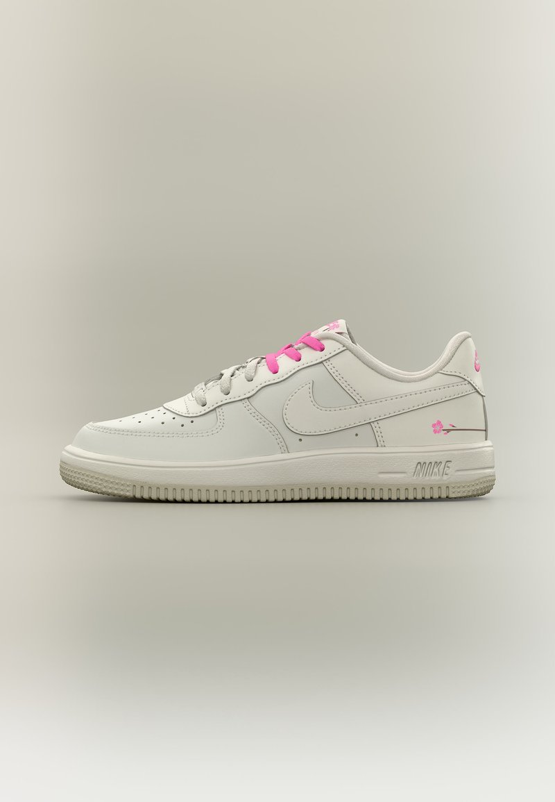 Λευκό χαμηλό αθλητικό παπούτσι Nike με ροζ κορδόνια και λεπτομέρειες λουλουδιών στη φτέρνα και στο πλάι, παρουσιάζεται σε ουδέτερο φόντο.