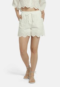 Witte scalloped shorts met uitgesneden oogjesontwerp, elastische tailleband en zijzakken. Gecombineerd met lichte sandaaltjes met banden.