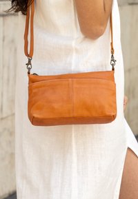 Tan läder crossbody-väska med rektangulär form, med dragkedjestängning och justerbar rem. Slät yta med synlig sömnad.