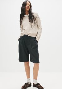 Maglione beige lavorato a maglia, pantaloni corti neri a righe e sneakers con motivo. Il sudore ha polsini a coste; i pantaloni corti presentano delle pieghe.