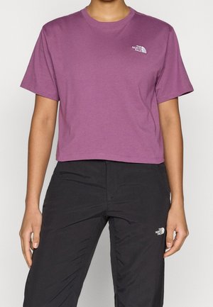 Osoba nosząca fioletowy krótki T-shirt z krótkim rękawem i czarne spodnie, oba z logo The North Face.