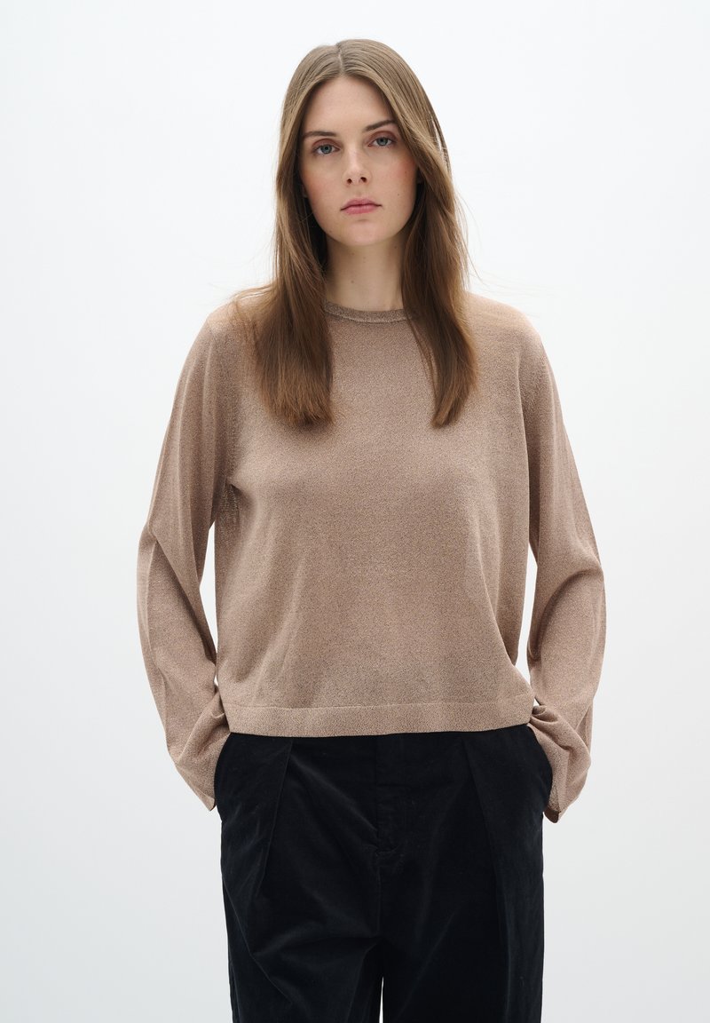 Maglione lungo color marrone chiaro, con maniche lunghe, una texture morbida, scollo a girocollo e una vestibilità morbida, abbinato a pantaloni neri scuri plisettati.