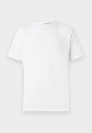 Camiseta de algodón blanca con cuello redondo y mangas cortas. Presenta un logo sutilmente en relieve en el pecho. Textura suave, corte estándar.