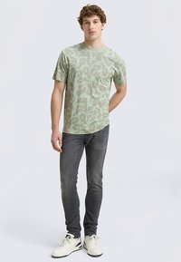 Heleheline heleroheline lühikeste varrukatega t-särk pikslilise kamuflaažimustriga, kombineeritud tumedate hallide teksade ja valgete tossudega.