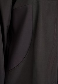 Schwarze Jacke mit glatter Außenfläche und einer strukturierten Taschenblende. Die Tasche hat eine abgerundete Form mit kontrastierendem, geripptem Stoff.