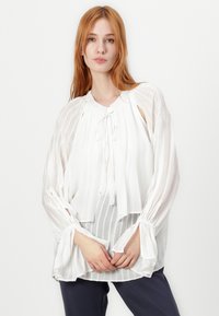 Blusa bianca con tessuto trasparente a strisce, scollo annodato con frange e maniche lunghe voluminose con polsini elasticizzati. Texture liscia.