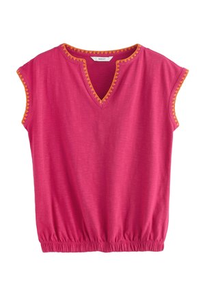Femme aux cheveux foncés portant un haut rose à col en V avec une bordure triangulaire orange le long de l'encolure et des manches sur un fond de ciel clair.